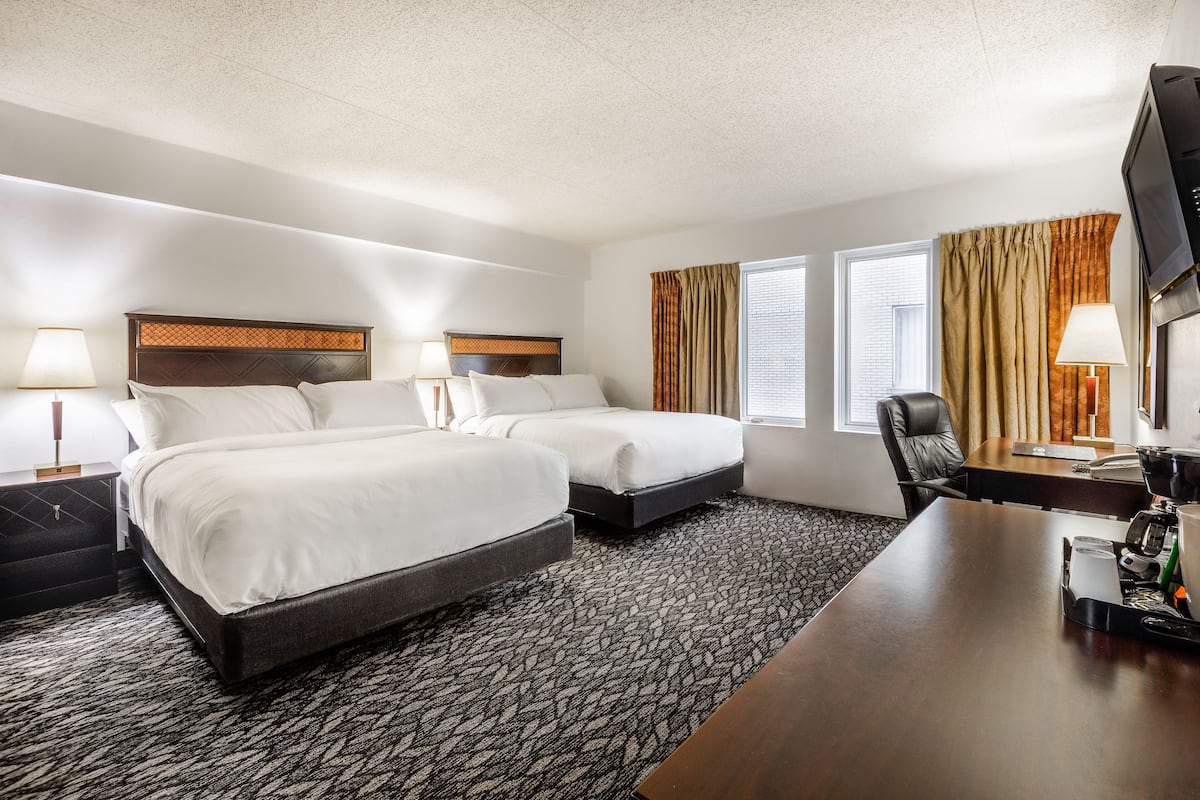 A hotel room with two beds, a desk, a chair, a television, and a window with curtains.