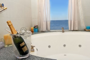 A bathtub with a view of the sea, a bottle of champagne, and a small flower vase.