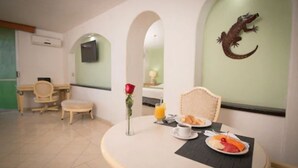 Un comedor con una mesa redonda, alimentos para el desayuno, una rosa y una decoración de reptil colgada en la pared.