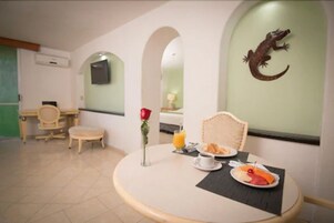 Uma sala de jantar com uma mesa redonda, itens de café da manhã, uma rosa e um ornamento de réptil fixado na parede.