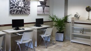 Una oficina moderna con dos escritorios, cada uno con un ordenador y una silla. Hay obras de arte decorativas en la pared y una planta en maceta.