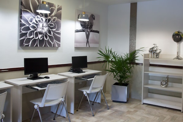 A modern office with two desks, each with a computer and a chair. There are decorative wall art pieces and a potted plant.