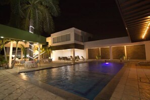 Un hôtel moderne doté d’une piscine, de chaises longues et d’un patio couvert.
