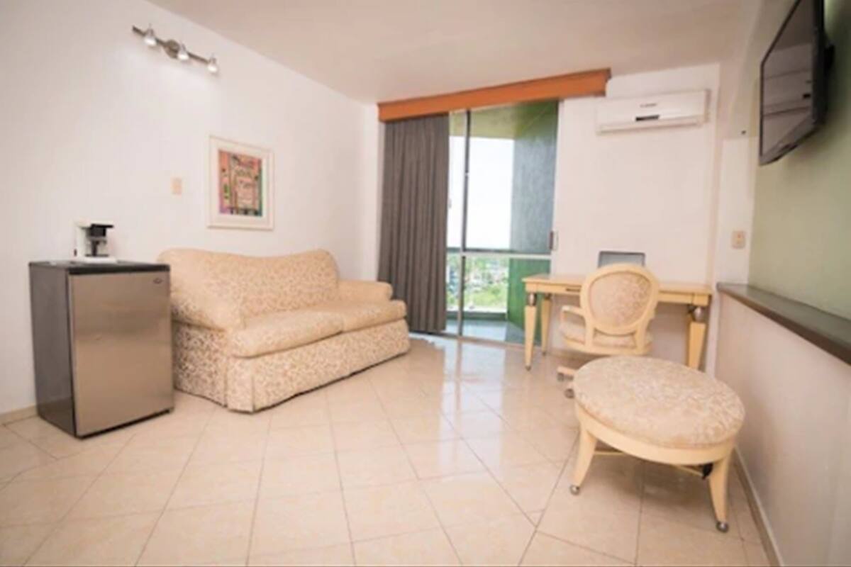 Un espacio habitable compacto con sofá, una mesita, una silla y un refrigerador.