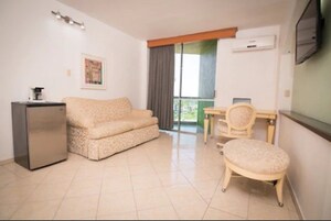 A compact living space with a sofa, a small table, a chair, and a refrigerator.