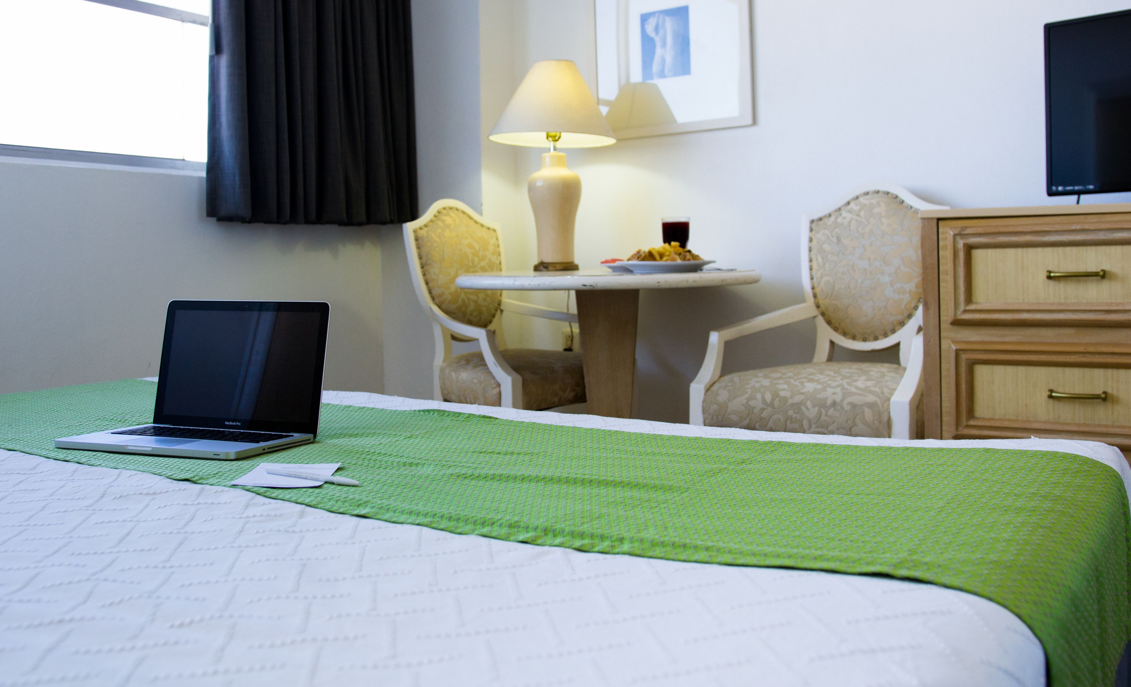 A hotel room with a bed, a desk with a lamp, a chair, and a television.