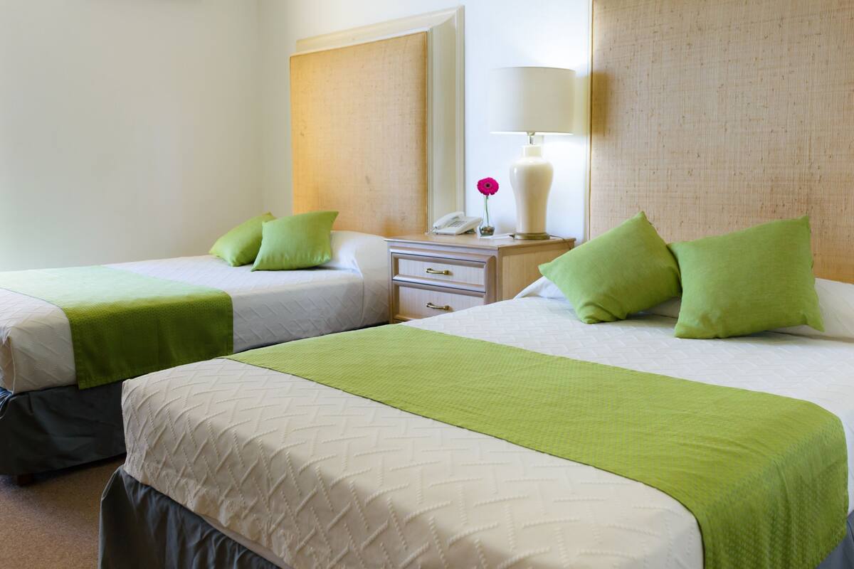 Dos camas individuales con ropa de cama verde, una mesita de noche con lámpara y un teléfono.