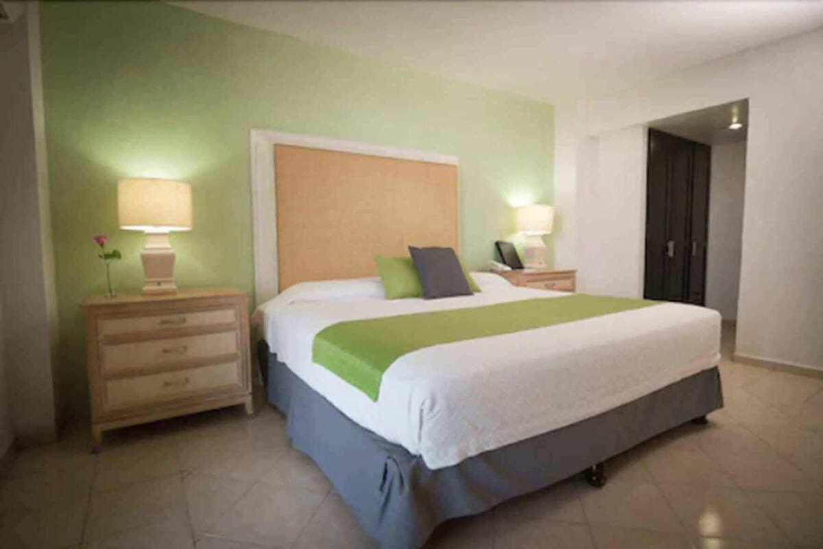 Un dormitorio con cama, mesitas de noche, lámpara y una puerta.