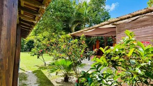 A covered outdoor area with a thatched roof, surrounded by lush greenery and flowering plants. - Pousada Aquarela (Porto Seguro)