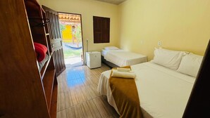 A room with two beds, a small table, a heater, and a door leading to an outdoor area. - Pousada Aquarela (Porto Seguro)