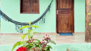 A house with a green exterior, two wooden doors, a hammock, and a small porch area with plants. - Pousada Aquarela (Porto Seguro)