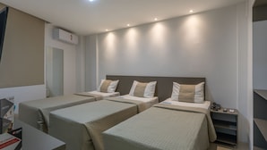 Une chambre d’hôtel avec trois lits simples, un petit bureau, une table de chevet avec un téléphone et un climatiseur fixé au mur.