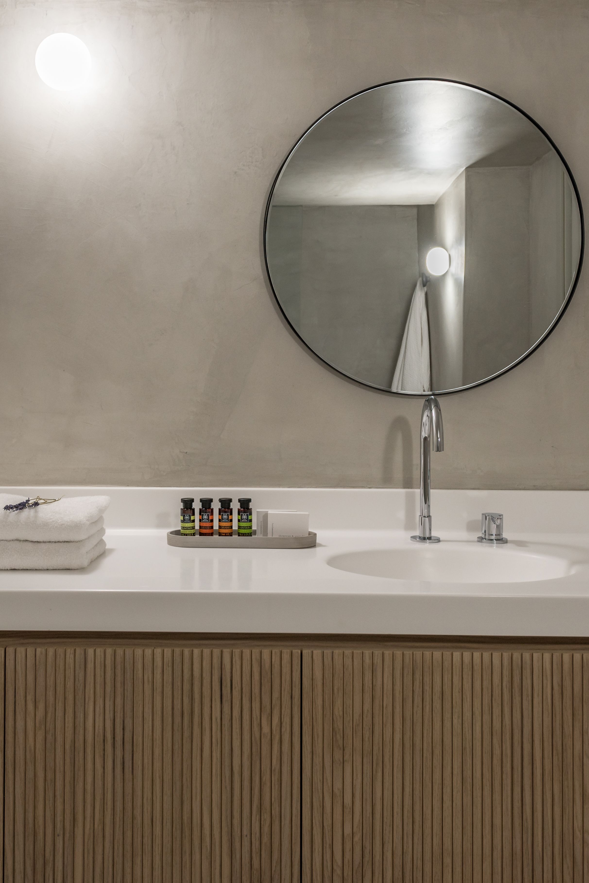 Un baño con un espejo redondo, un lavabo blanco y un perchero para toallas.
