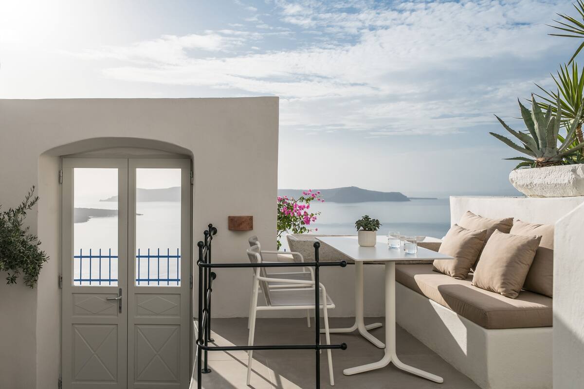 Uma varanda com porta branca, mesa, sofá e vista para o mar.