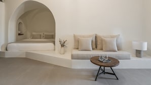 Un dormitorio minimalista con cama, sofá, una mesita con vasos y un jarrón de flores.