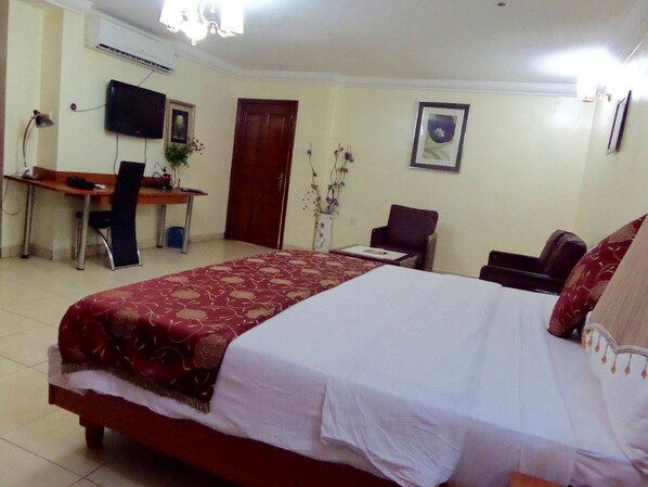 A hotel room with a large bed, a desk with a chair, a television, and a door. - Deen Apartment Services (Lagos)