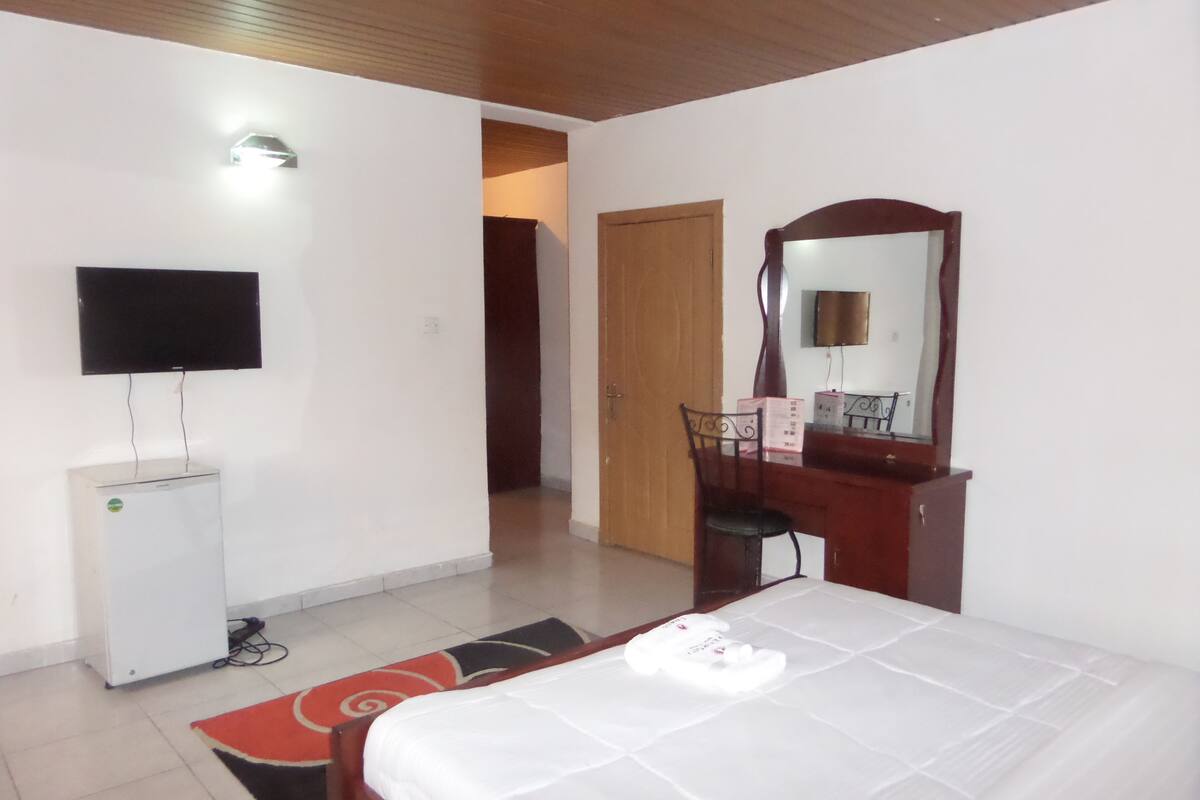 A hotel room with a bed, a desk, a chair, a TV, and a wardrobe.