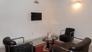 Ein modernes Wohnzimmer mit einem an der Wand befestigten Flachbildfernseher, einem runden Couchtisch und vier schwarzen Ledersesseln, die darum platziert sind.