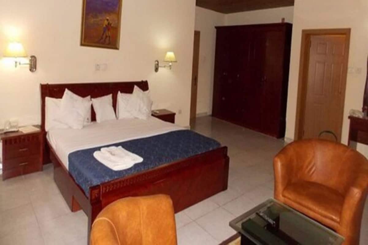 A hotel room with a large bed, a wooden ceiling, a painting on the wall, and a brown leather chair.