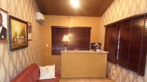 Ein Zimmer mit Holzboden, einem roten Sofa, einem Schreibtisch mit Lampe und einem Fenster mit Jalousien.