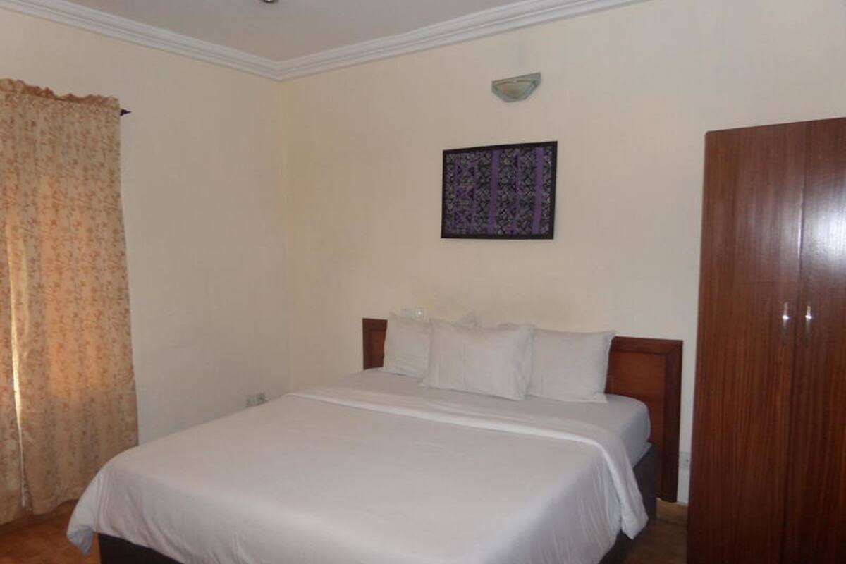 A bedroom with a large bed, a wooden wardrobe, and a wall-mounted artwork.