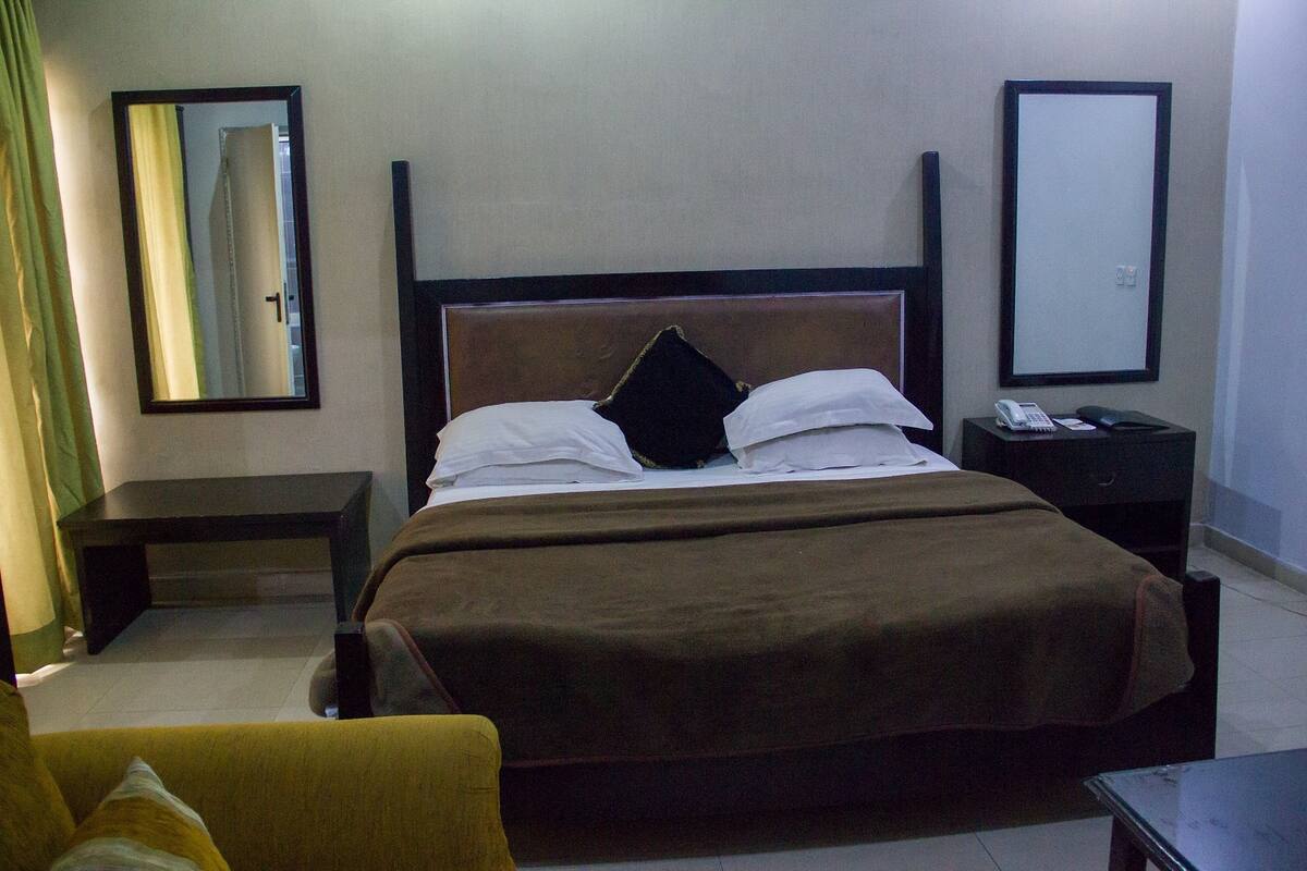 A hotel room with a bed, a bedside table, a chair, and a mirror.
