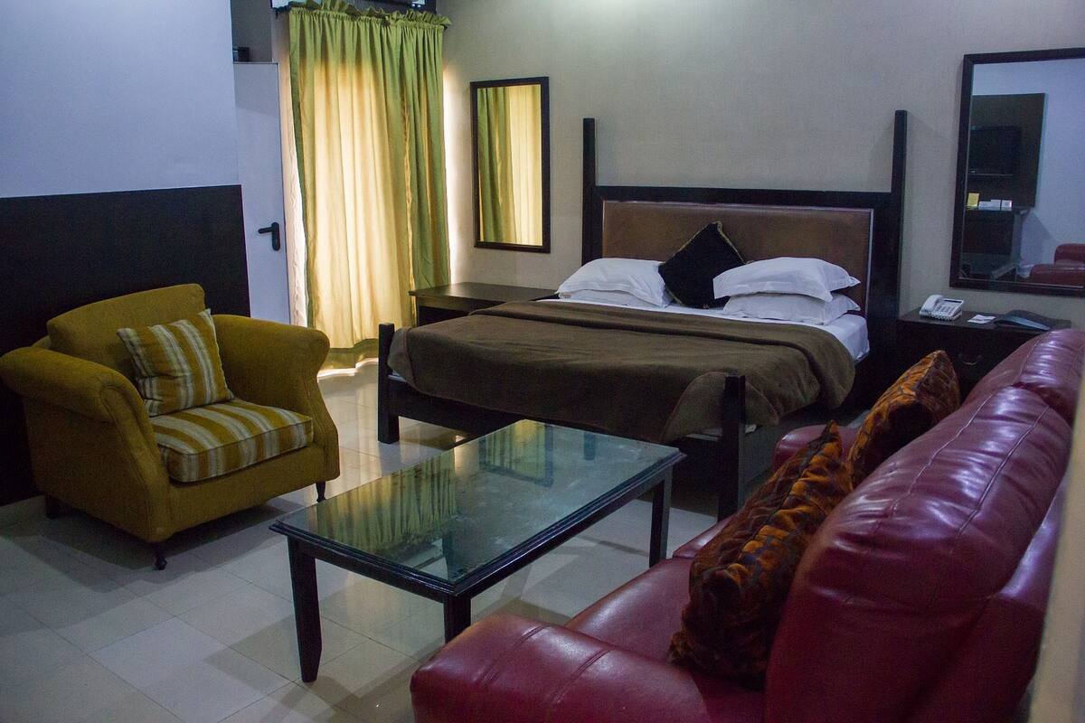 A hotel room with a bed, a sofa, a chair, and a glass table.