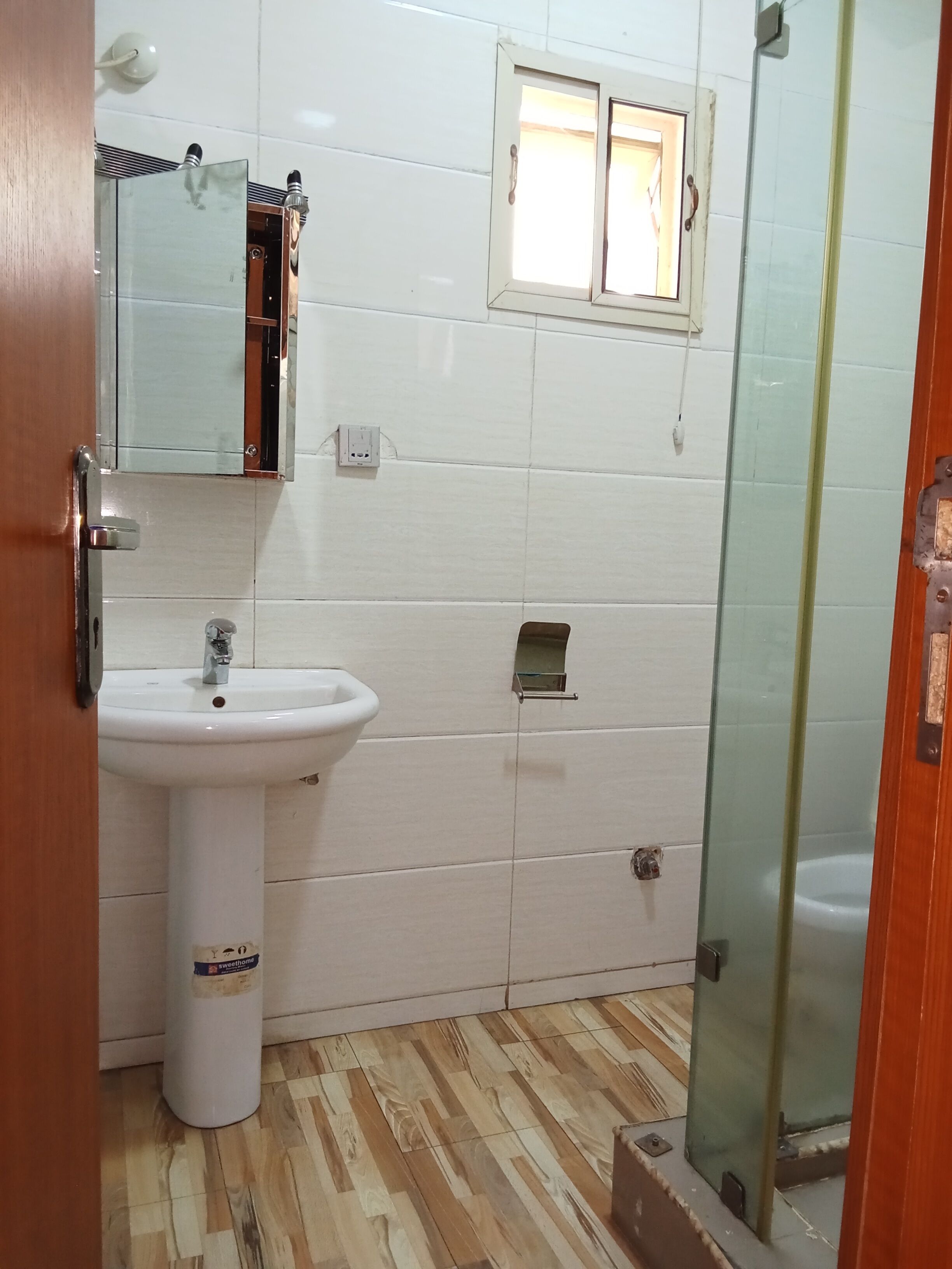 A bathroom with a white sink, a mirror, a window, and a shower area.