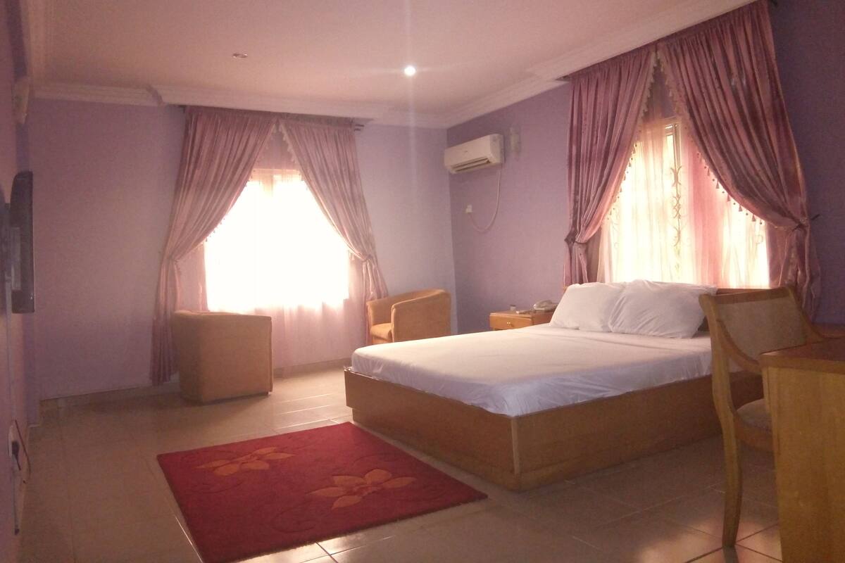 Une chambre à coucher avec un lit, une chaise, une table de chevet et un tapis rouge.