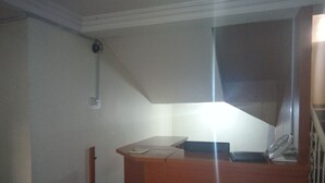 Una habitación pequeña y tenuemente iluminada, con un escritorio de madera, un teléfono y una lámpara fijada a la pared.
