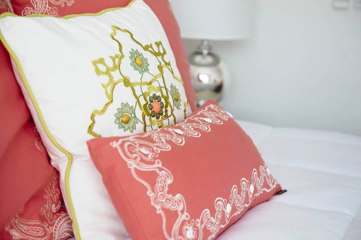 Uma cama com dois travesseiros, um branco com bordado amarelo e outro vermelho com estampas brancas.
