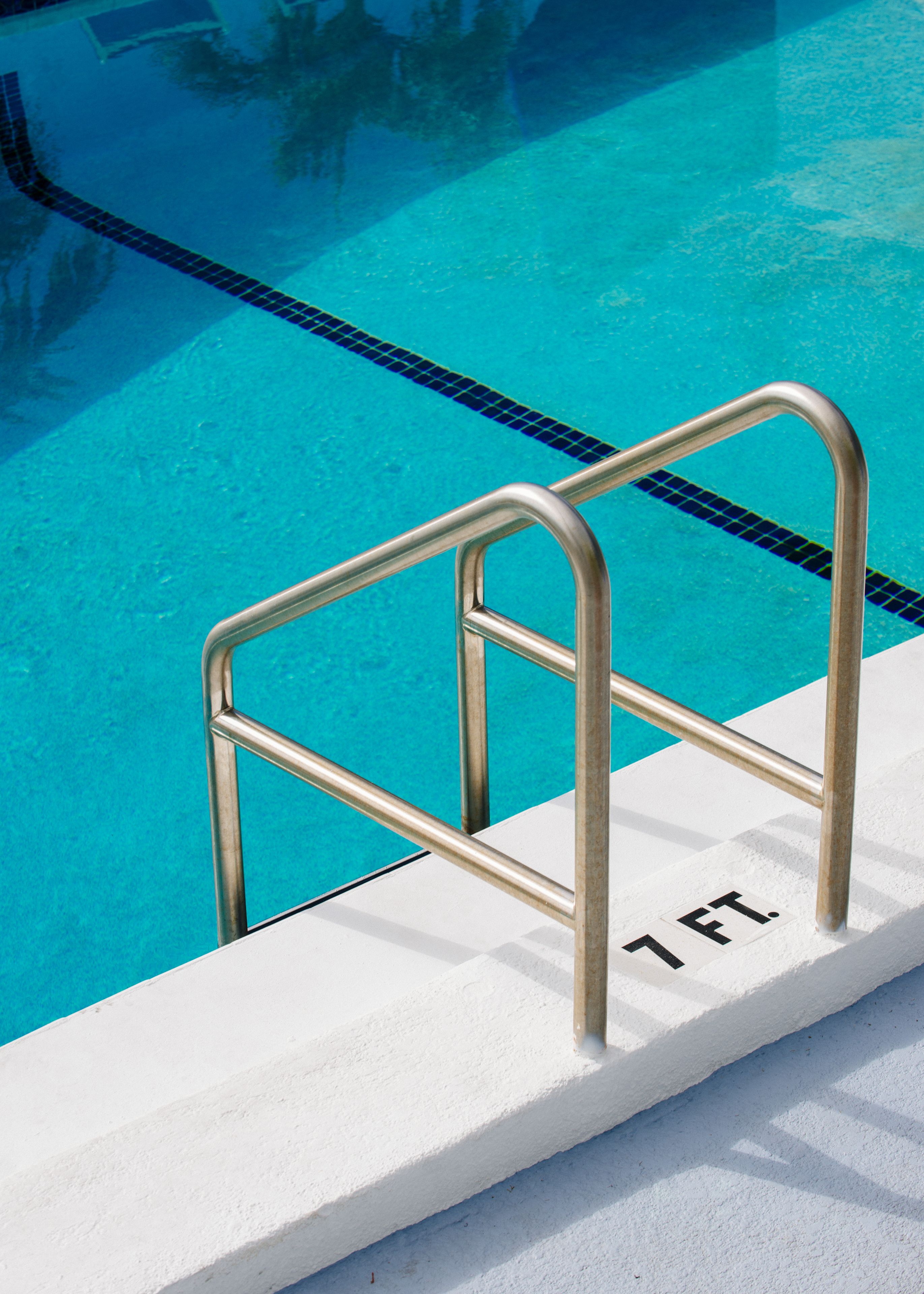 En swimmingpool med klart, blått vatten, en metallstege och en vit kant med en svart markering som visar ”1 FT” (1 fot).