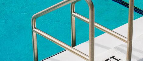 En swimmingpool med klart, blått vatten, en metallstege och en vit kant med en svart markering som visar ”1 FT” (1 fot).
