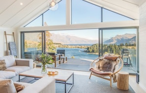 A spacious room with a large sliding glass door leading to a scenic mountain view. Inside, there is a sofa, a chair, and a coffee table. - Braeside (Queenstown)