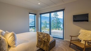 Une chambre avec un grand lit, une chaise, un téléviseur et une vue sur un lac et des montagnes.