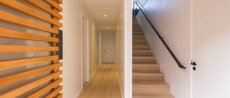 A hallway with wooden slats on one side and a staircase with a black railing leading to a door.