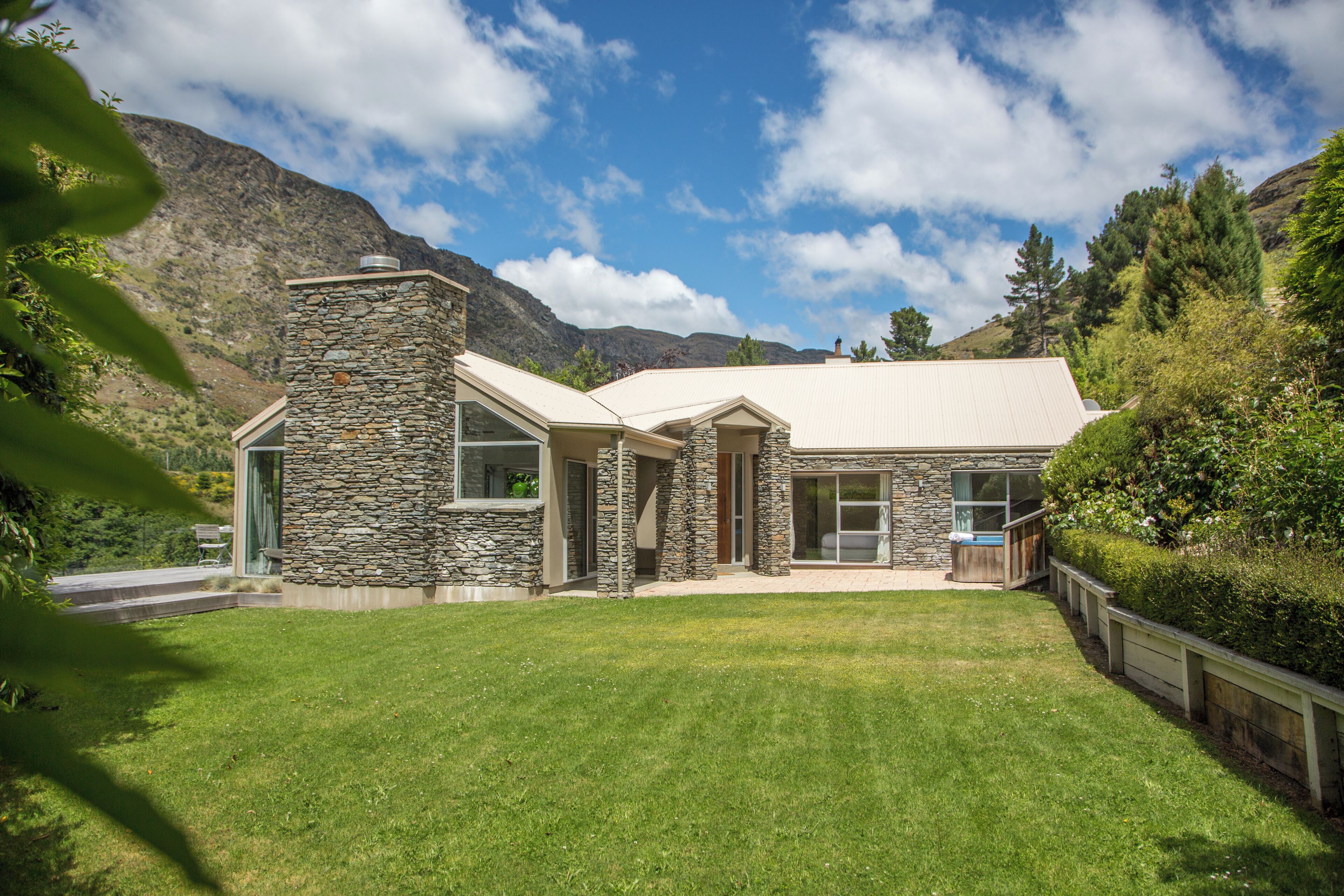 A modern house with stone walls, a sloped roof, and a well-maintained lawn.