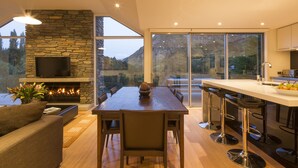 A modern dining area with a stone fireplace, a television, and a large window offering a mountain view. - Riverview Retreat (Arthur's Point)