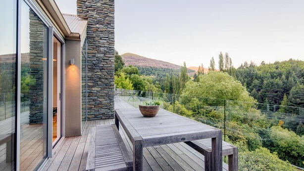 A wooden deck with a stone wall and a table with a potted plant. - Riverview Retreat (Arthur's Point)