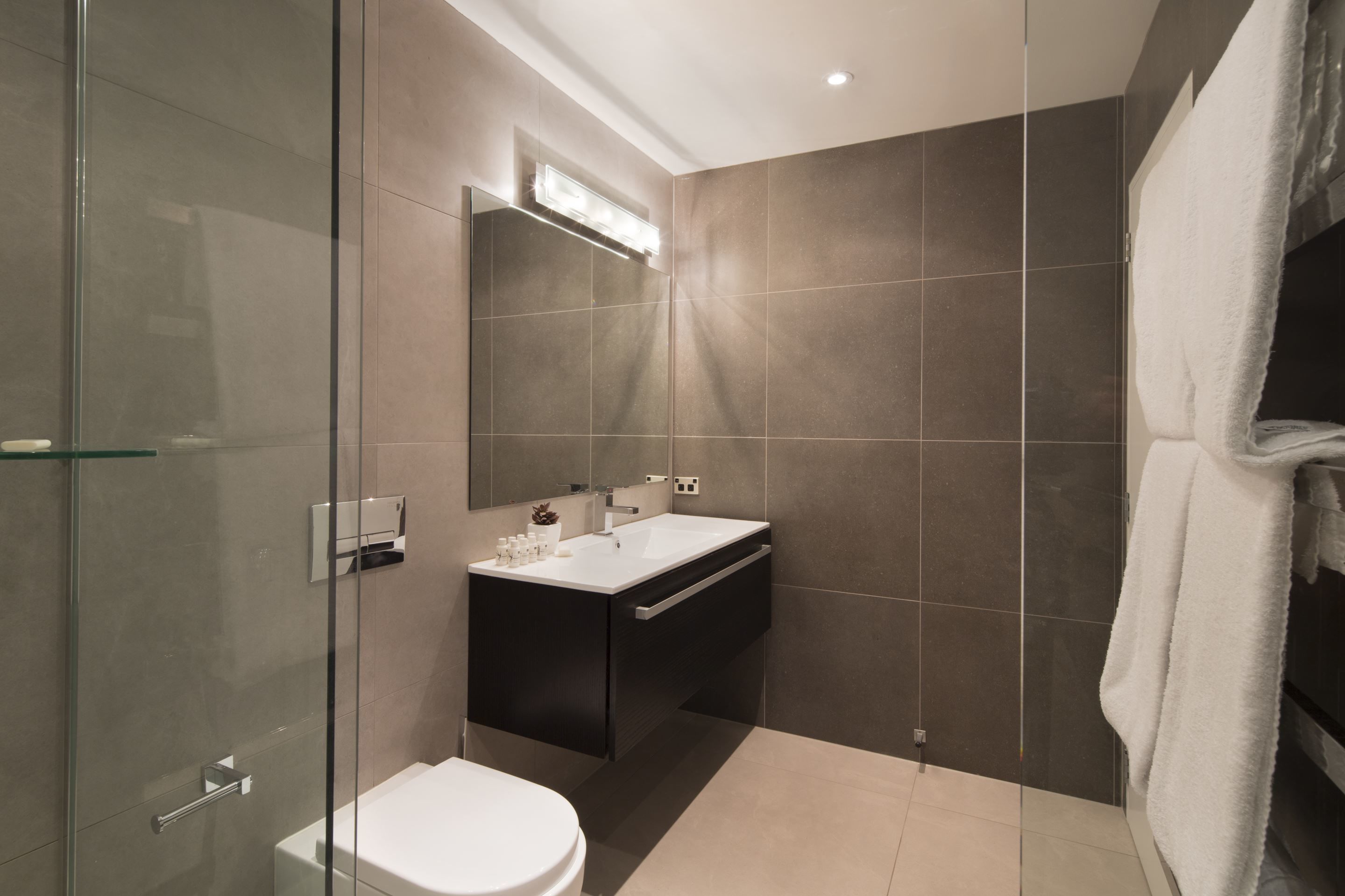 Une salle de bain moderne avec une douche à parois de verre, des toilettes blanches, un meuble-lavabo avec un miroir et une serviette accrochée au mur.
