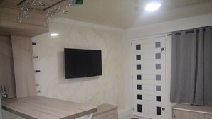 Un baño moderno con lavamanos, inodoro y ducha. Hay un televisor montado en la pared y una puerta con ventanal.