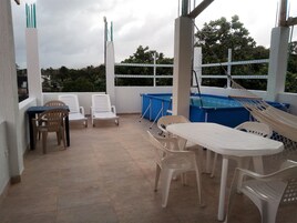Un espacio exterior cubierto con piscina, sillas de descanso y una mesa.