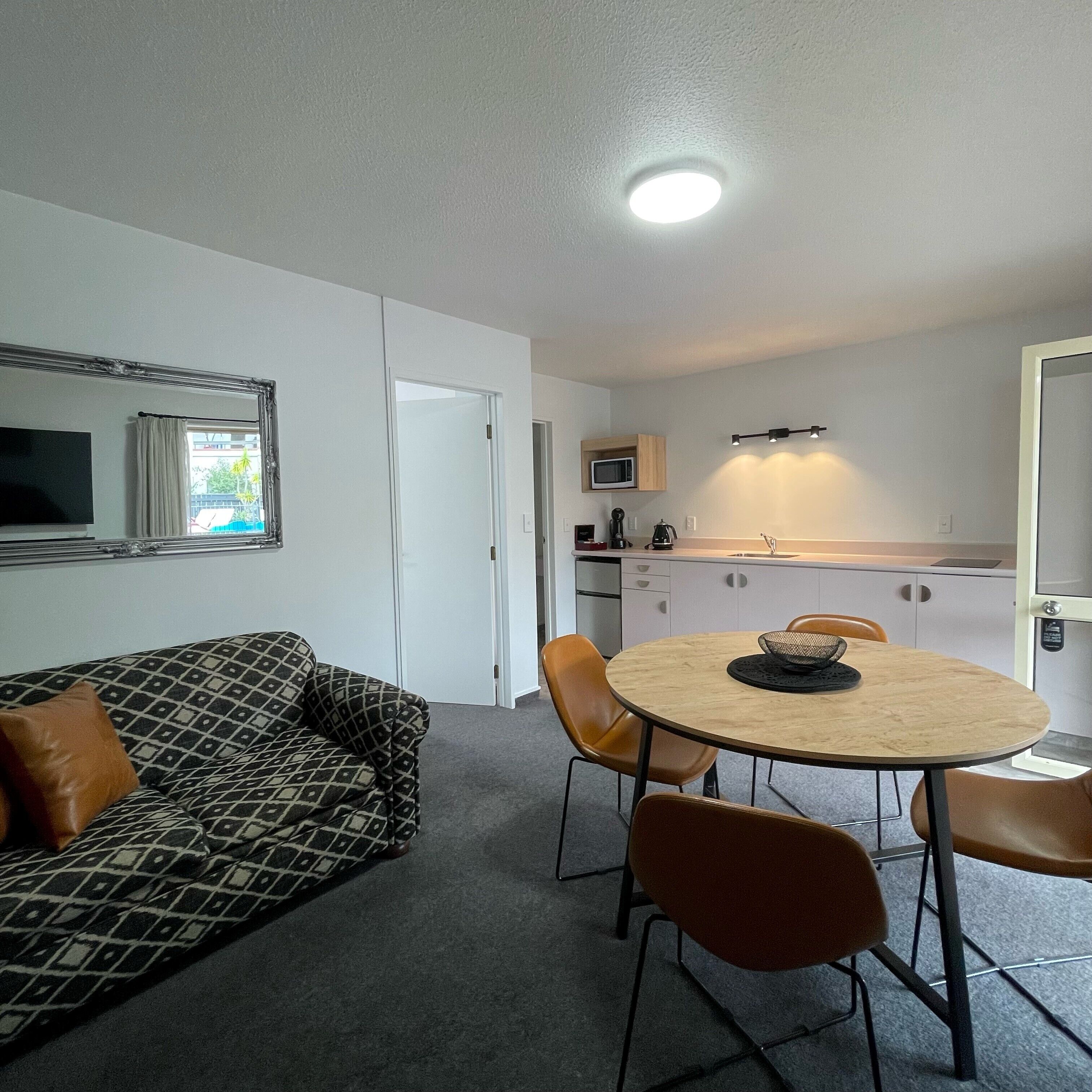 Un espacio habitable compacto con sofá, una mesa de comedor con sillas, una kitchenette y un televisor.