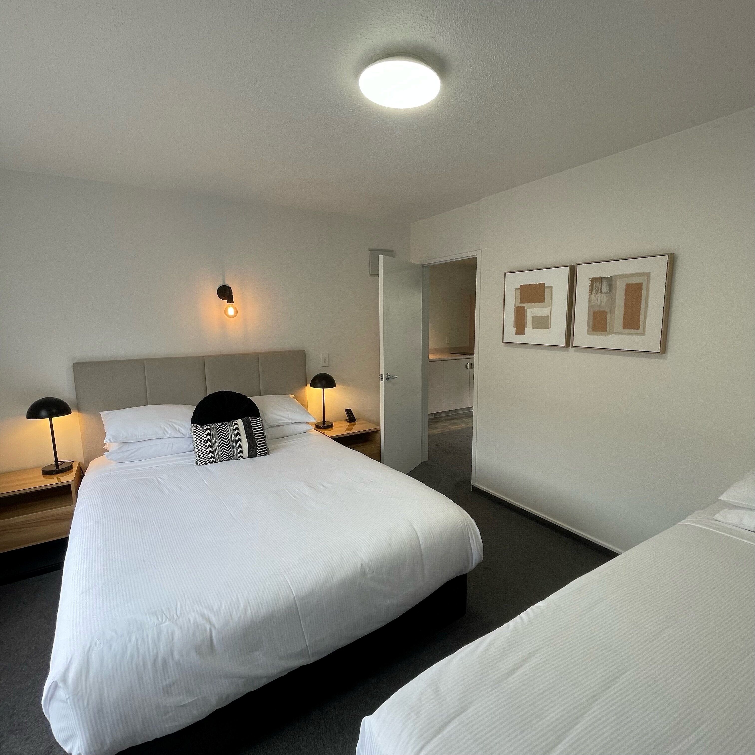 A hotel room with a large bed, two bedside tables, a nightstand, a wall-mounted light, and a door leading to a bathroom.