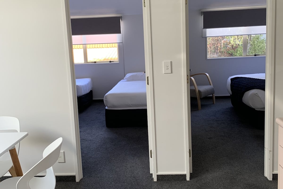A compact room with a white desk, two single beds, and a window with a view of trees.
