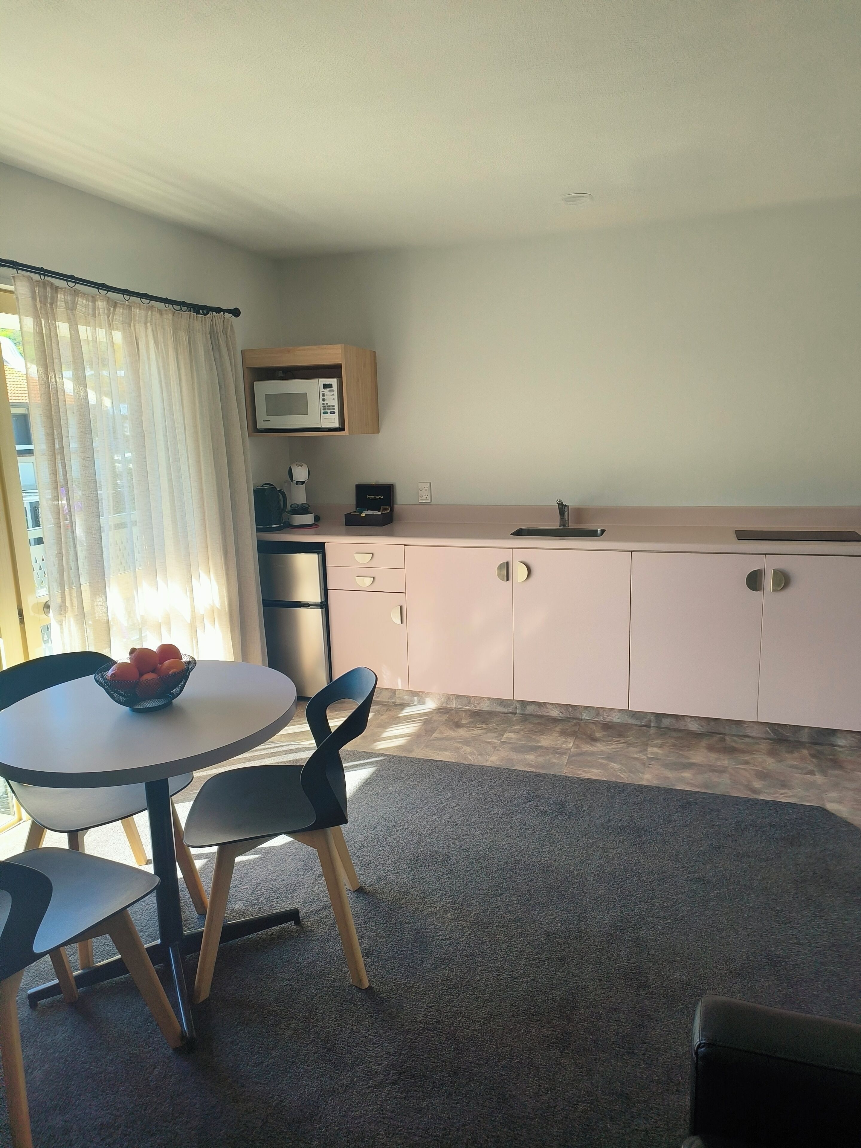 A compact kitchen with a microwave, coffee maker, and a sink. There is a round table with a bowl of fruit and two chairs.
