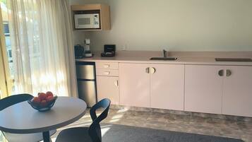 A compact kitchen with a microwave, coffee maker, and a sink. There is a round table with a bowl of fruit and two chairs.
