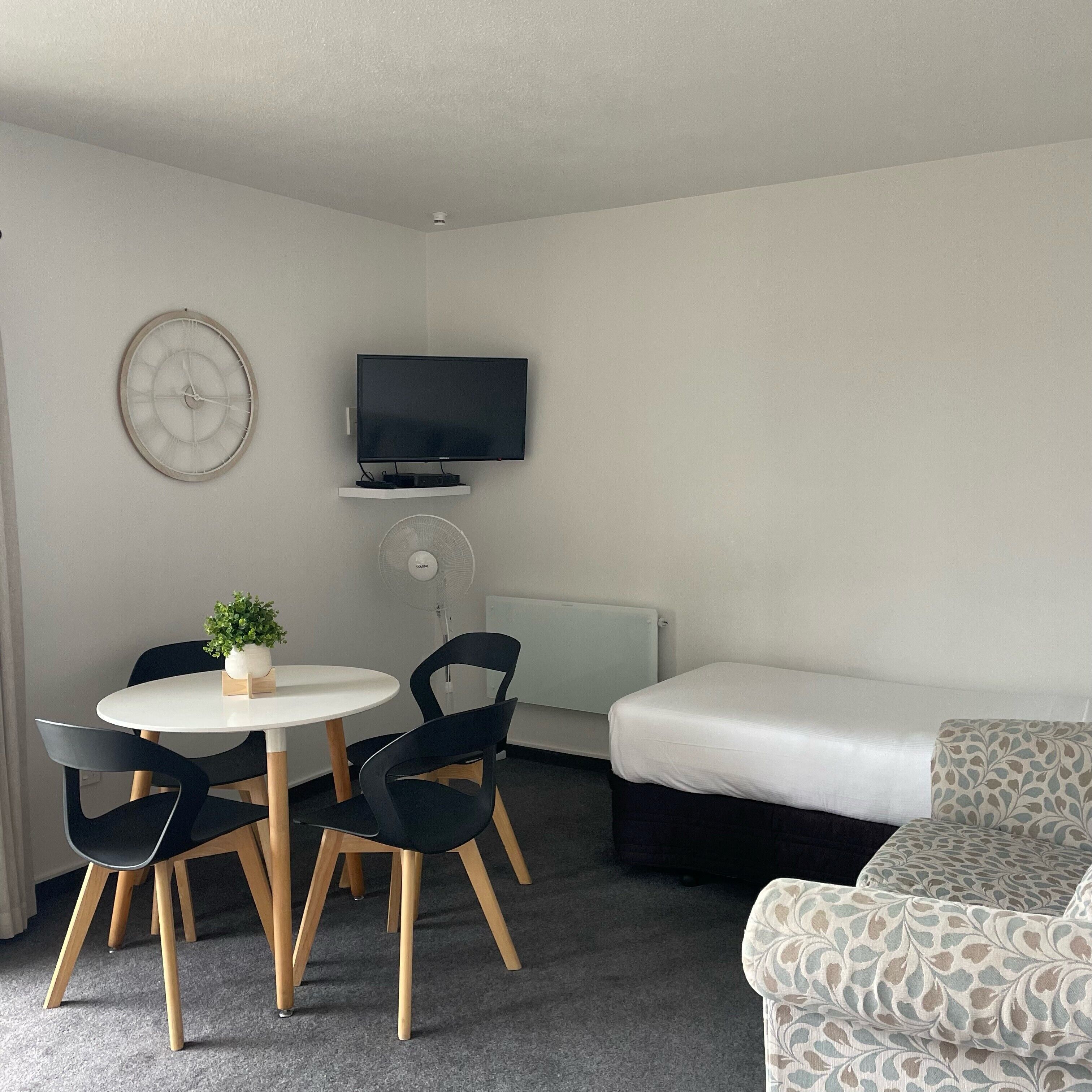Una habitación de hotel con una mesa redonda, dos sillas, un televisor, una cama y un radiador.