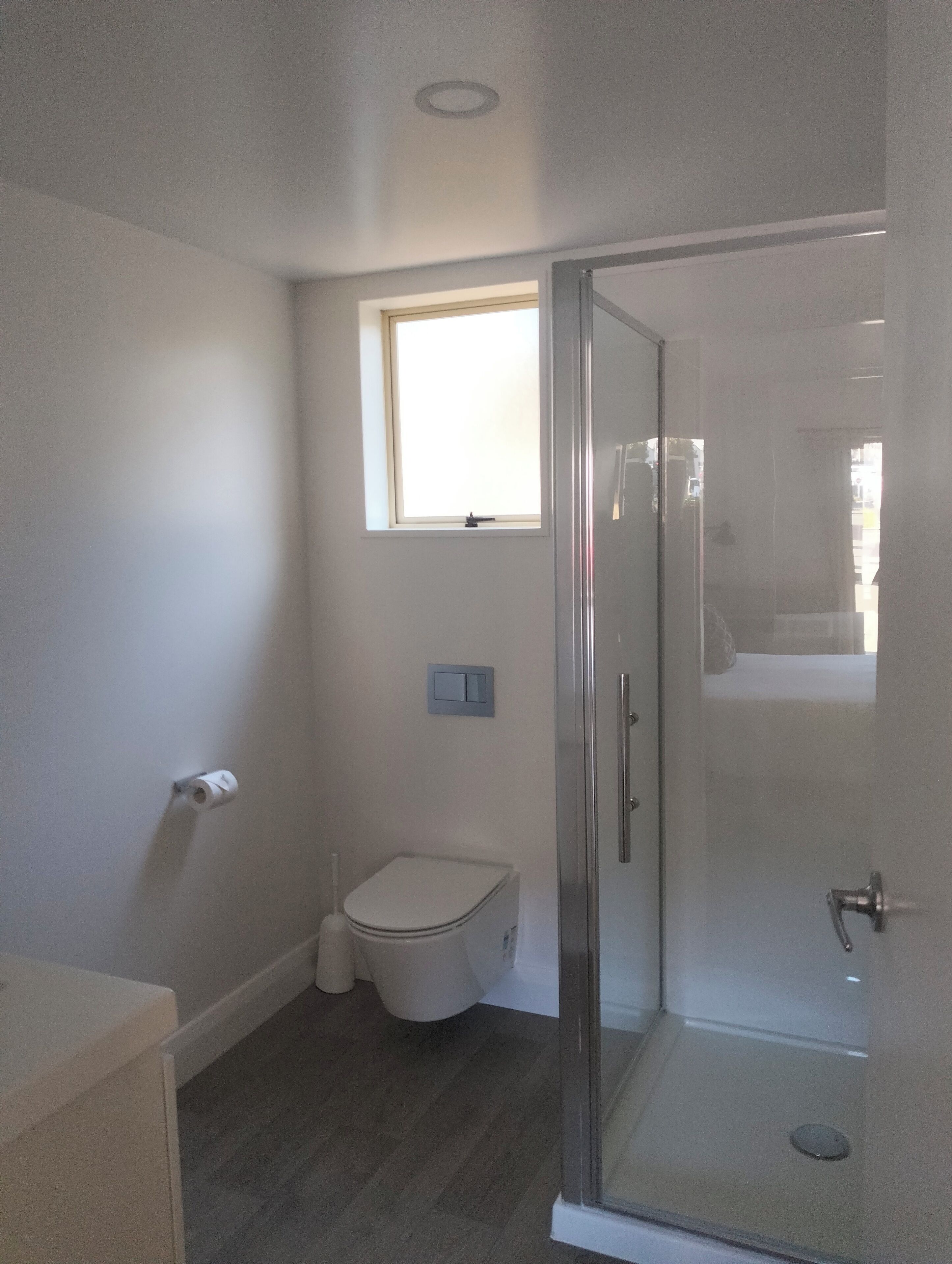 A bathroom with a toilet, a small window, and a glass shower enclosure.