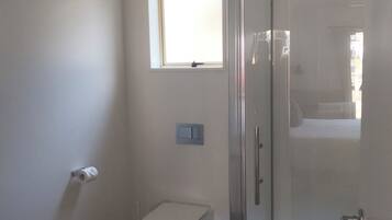 A bathroom with a toilet, a small window, and a glass shower enclosure.